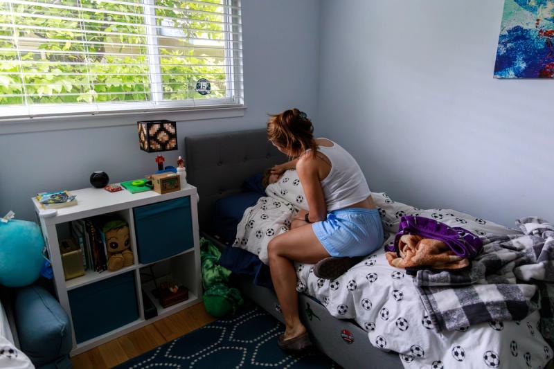 A parent leans over a child in a bed with soccer ball sheets in a brightly lit child's room.