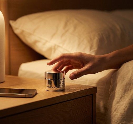Hand reaching for a Proven night‑repair cream jar on a bedside table.