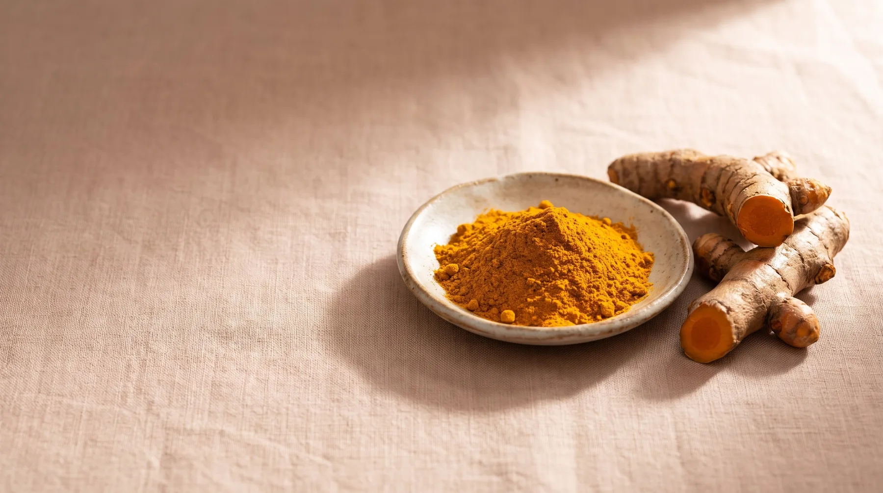 Curcumin extract — a dish of golden turmeric powder beside fresh turmeric root on warm linen