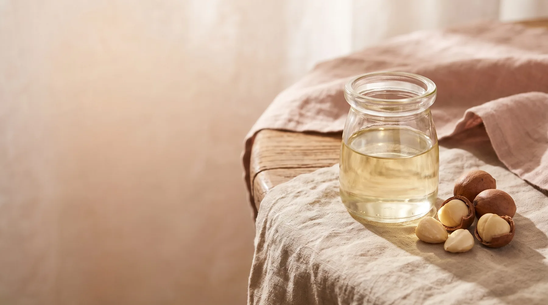 Marula oil — a glass vessel of pale-gold marula oil beside marula nuts on warm linen