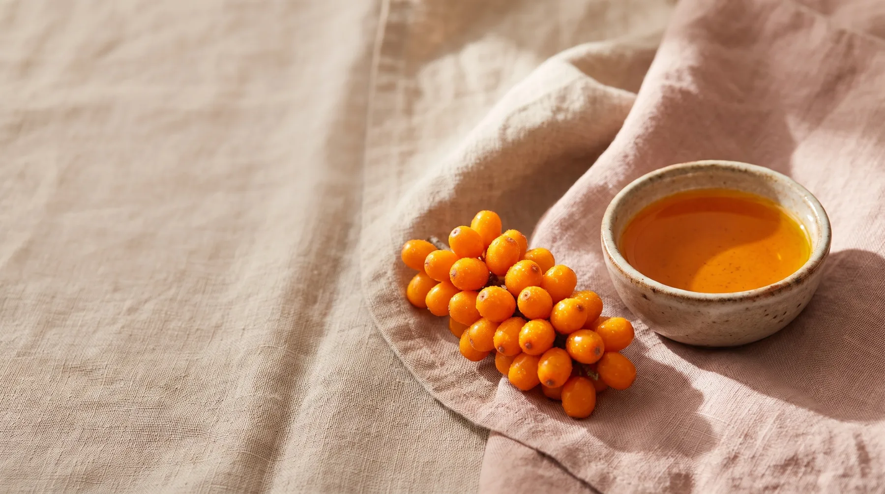 Sea buckthorn — vivid orange sea-buckthorn berries beside a vessel of orange oil on warm linen