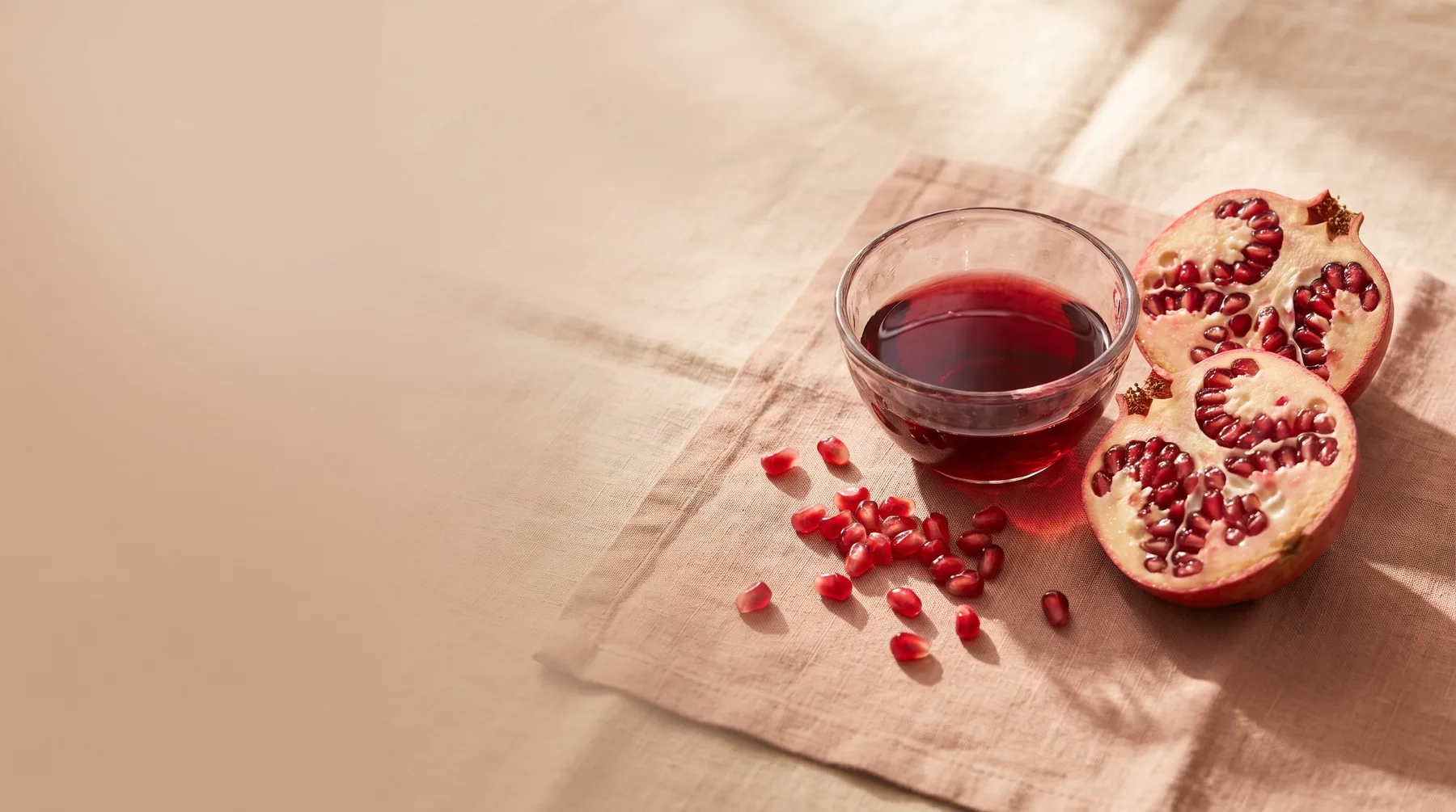 Pomegranate extract — a vessel of ruby extract beside a halved pomegranate and arils on warm linen