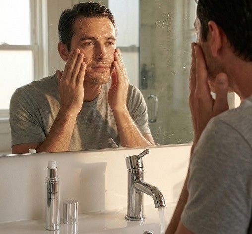 Man applying Proven cleanser and moisturizer in front of a bathroom mirror during his morning routine.