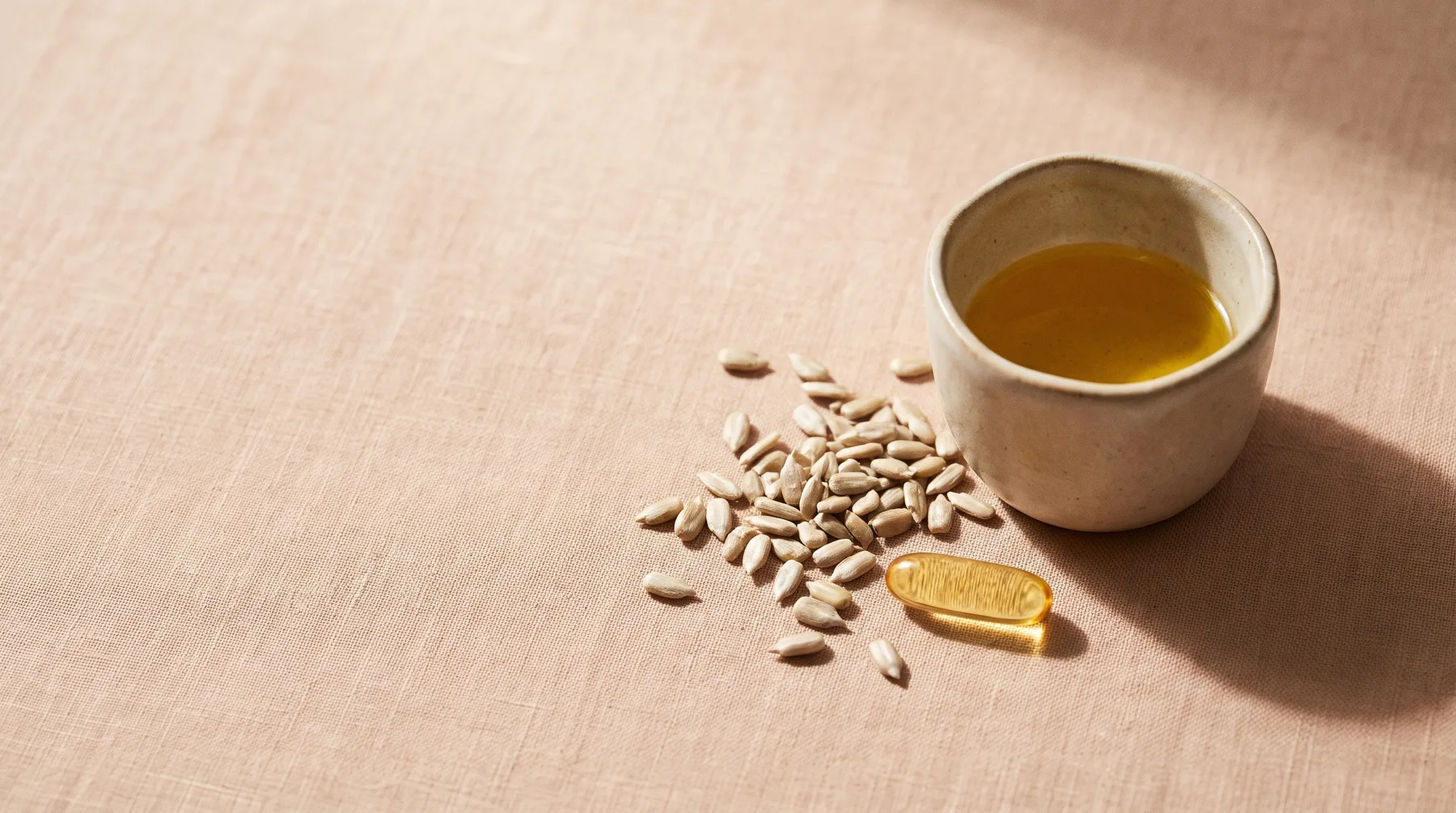 Vitamin E — a vessel of golden vitamin E oil beside sunflower seeds and a softgel on warm linen