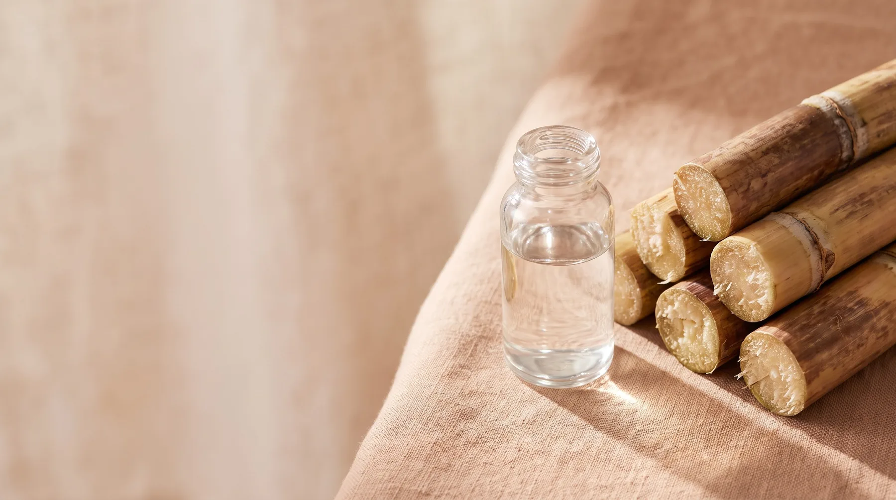 Glycolic acid — a clear vessel of glycolic acid beside cut sugarcane on warm linen