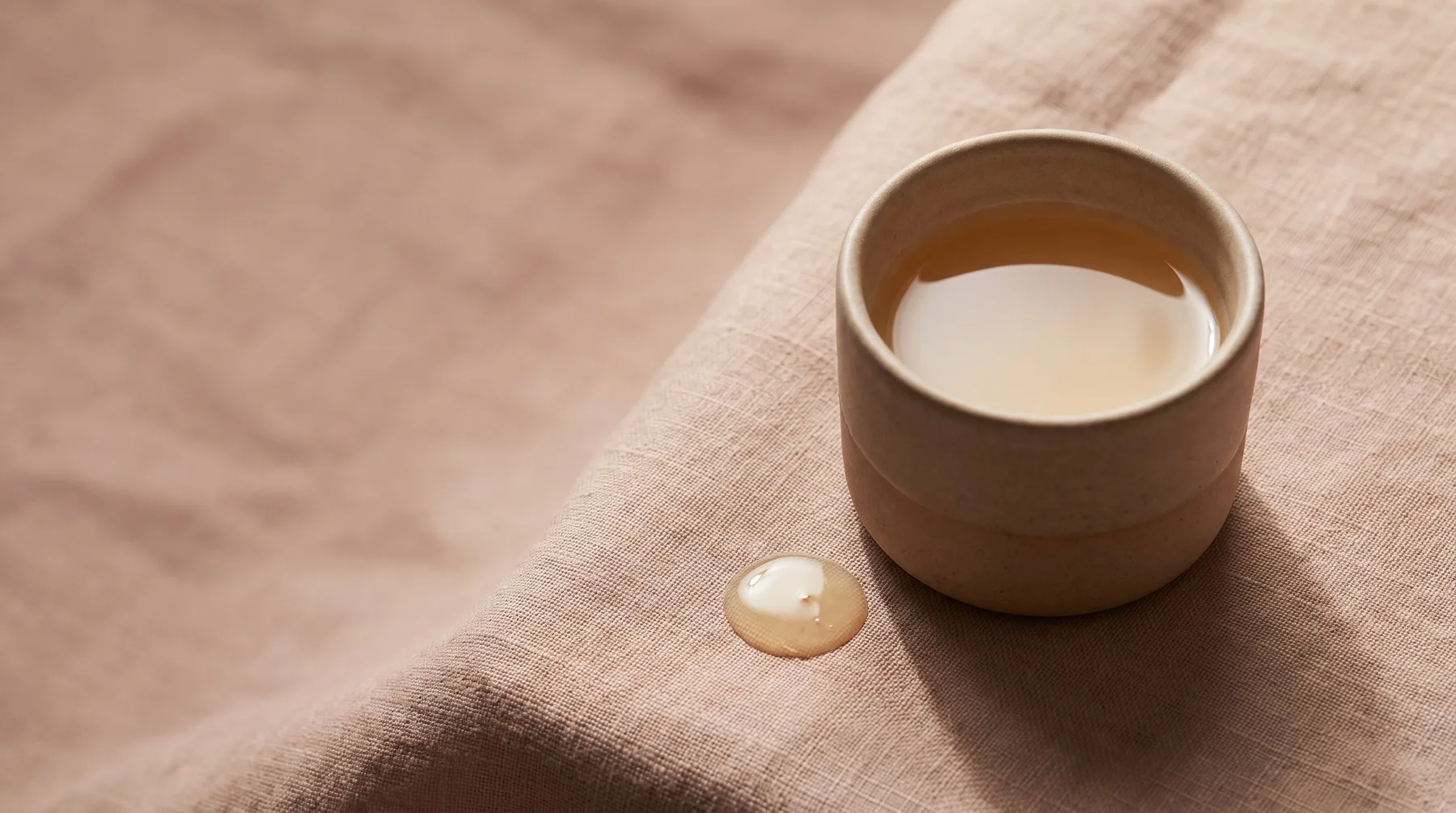 Granactive retinoid — a vessel of golden-amber retinoid serum with a droplet on warm linen