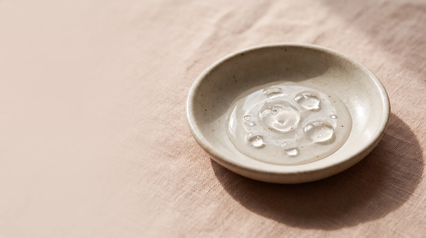 Hyaluronic acid — a dish of clear glossy hyaluronic-acid gel with droplets on warm linen