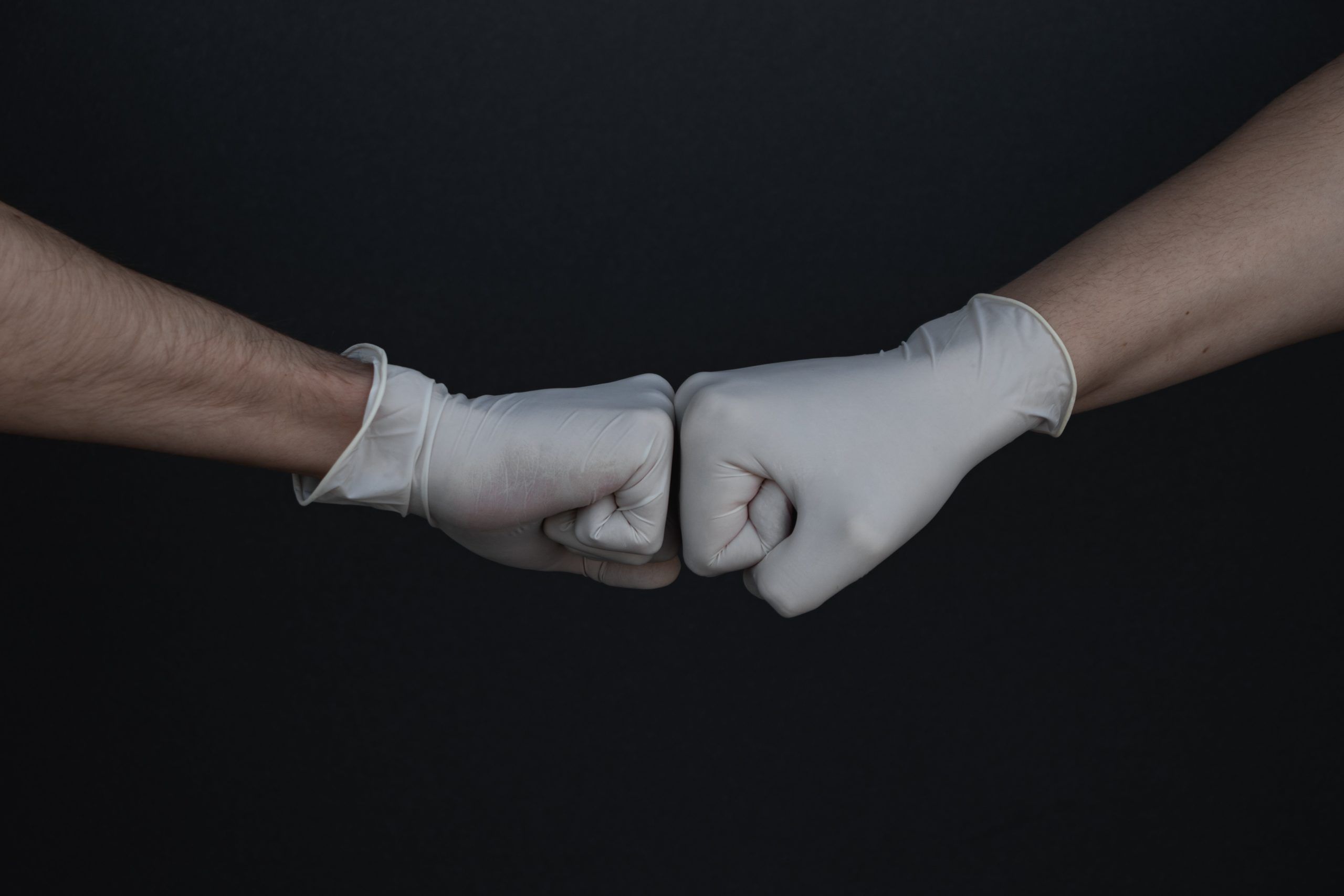 Two hands wearing rubber gloves fist bumping, representing team work to manage inventory in a surgical case.