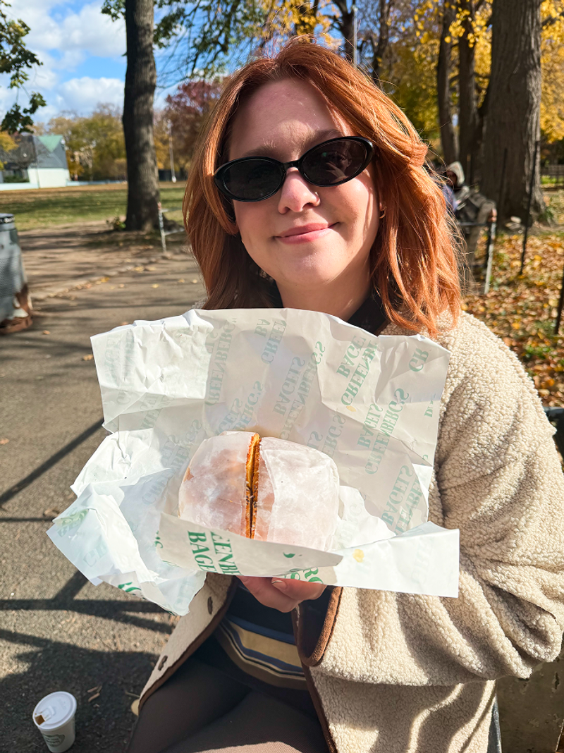 maddie showing a breakfast sandwich at a park in new york city