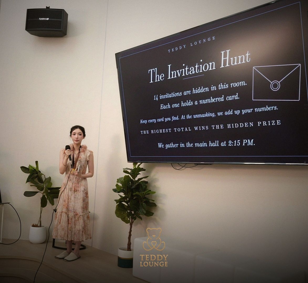 A host explains Teddy Lounge’s Invitation Hunt game on a large screen.