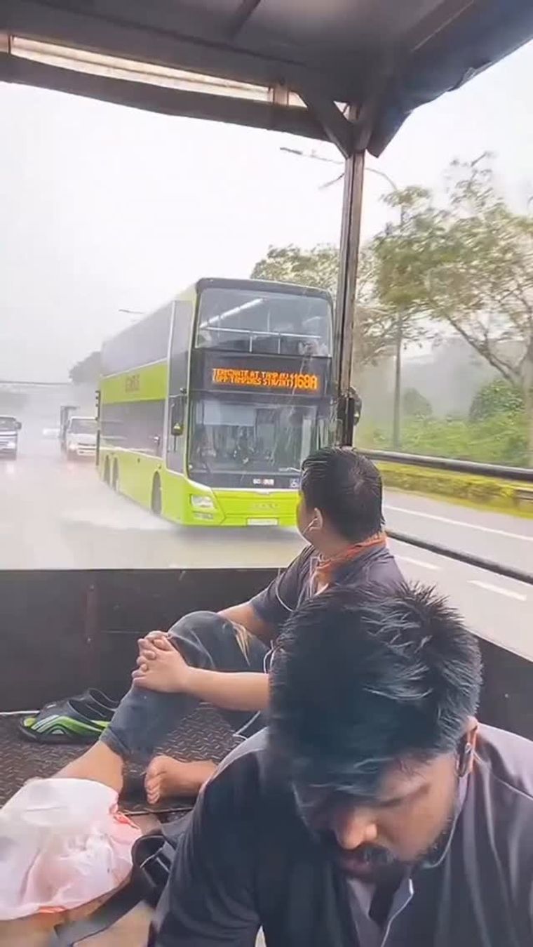 Passengers ride in open-backed vehicle as bus passes during heavy rain