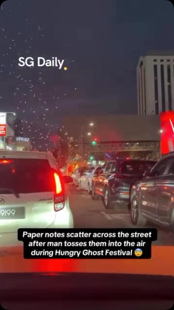 Paper notes scatter across the street after man tosses them into the air during Hungry Ghost Festival