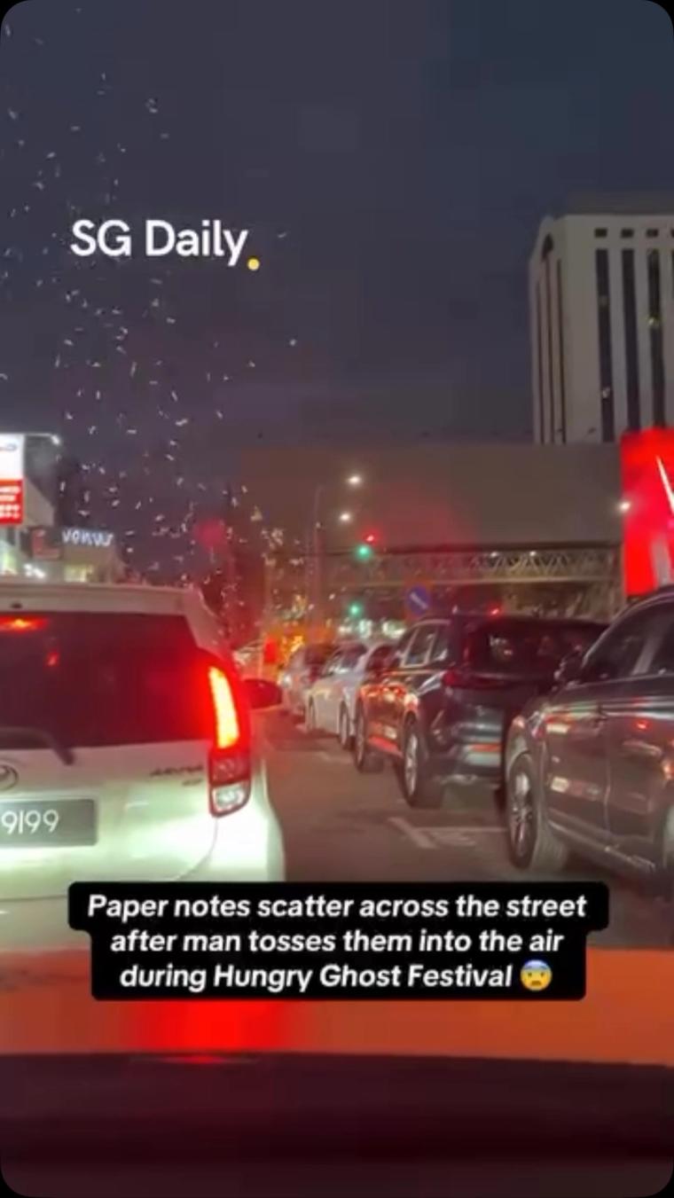 Paper notes scatter across the street after man tosses them into the air during Hungry Ghost Festival