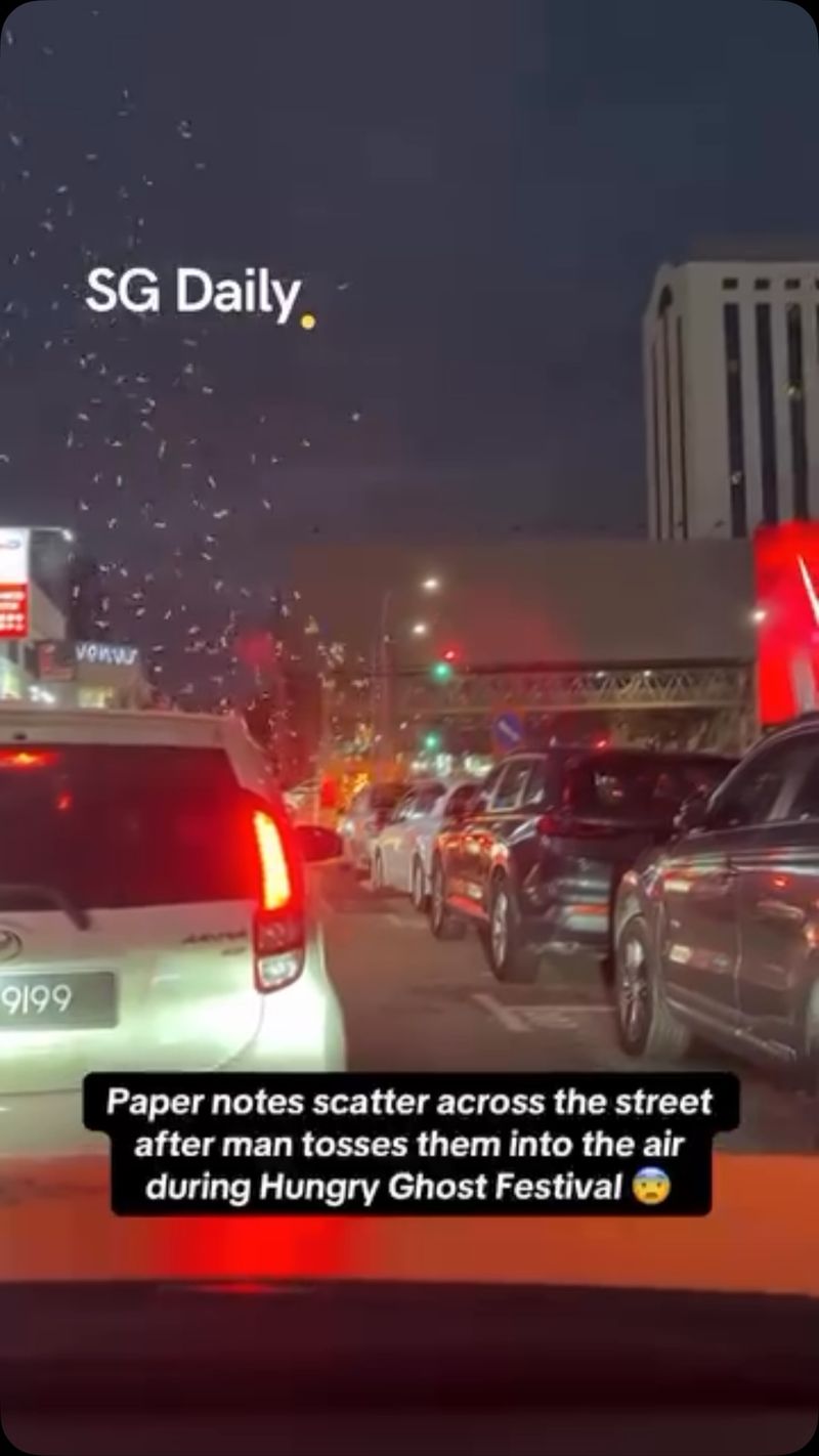 Paper notes scatter across the street after man tosses them into the air during Hungry Ghost Festival