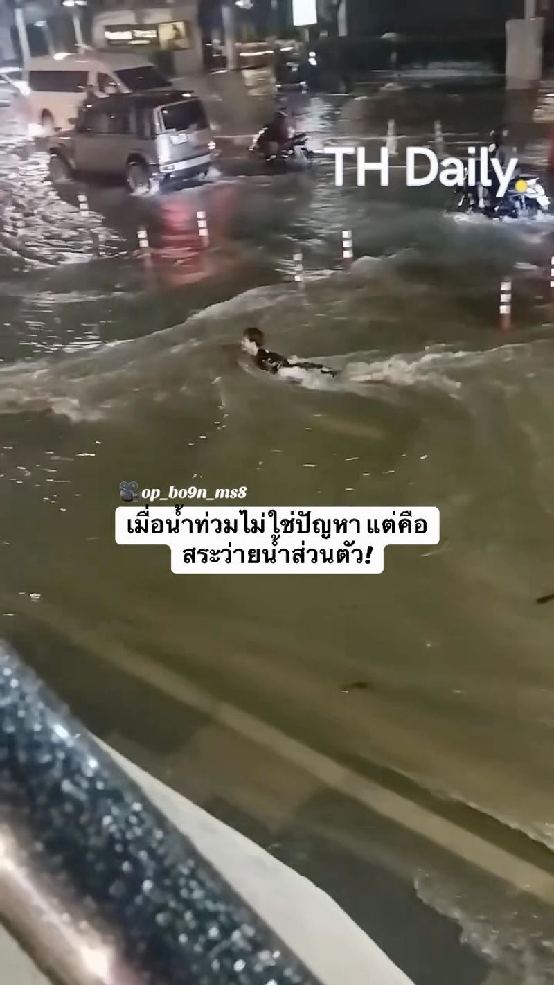 Person swims along a flooded road beside traffic