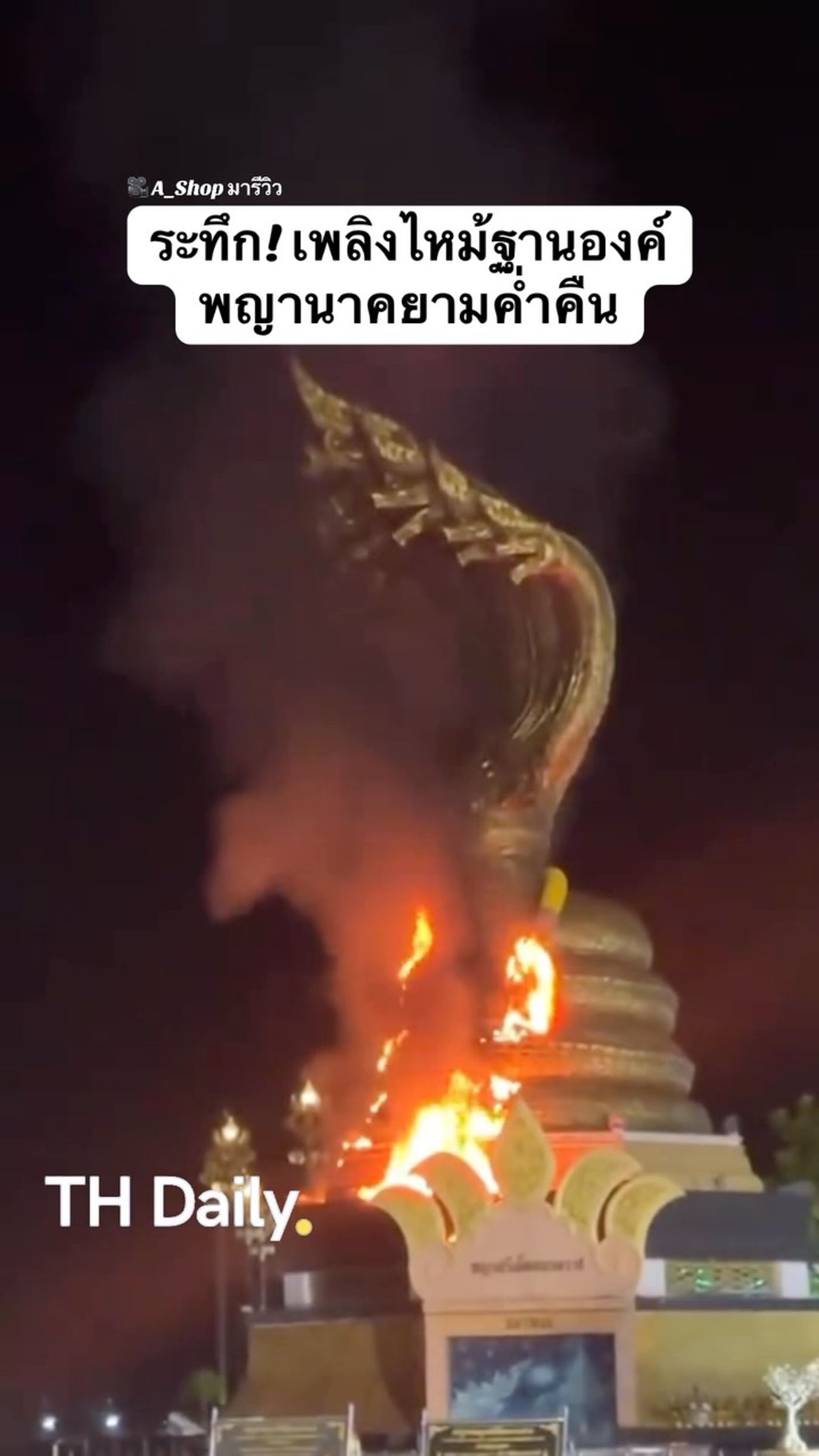 Fire burns at the base of a Naga statue at night
