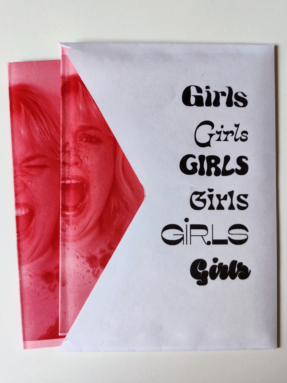 White cover sheet printed with “Girls” in six different display typefaces, slid over the pink screaming-woman print