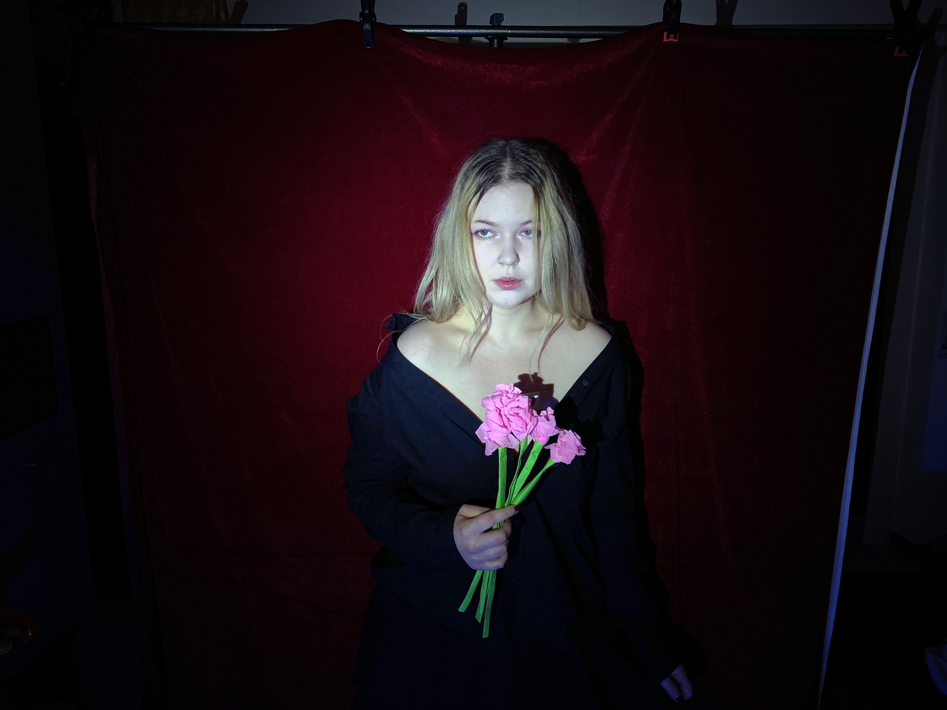 Standing in black against a red velvet backdrop, holding a small bunch of pink carnations