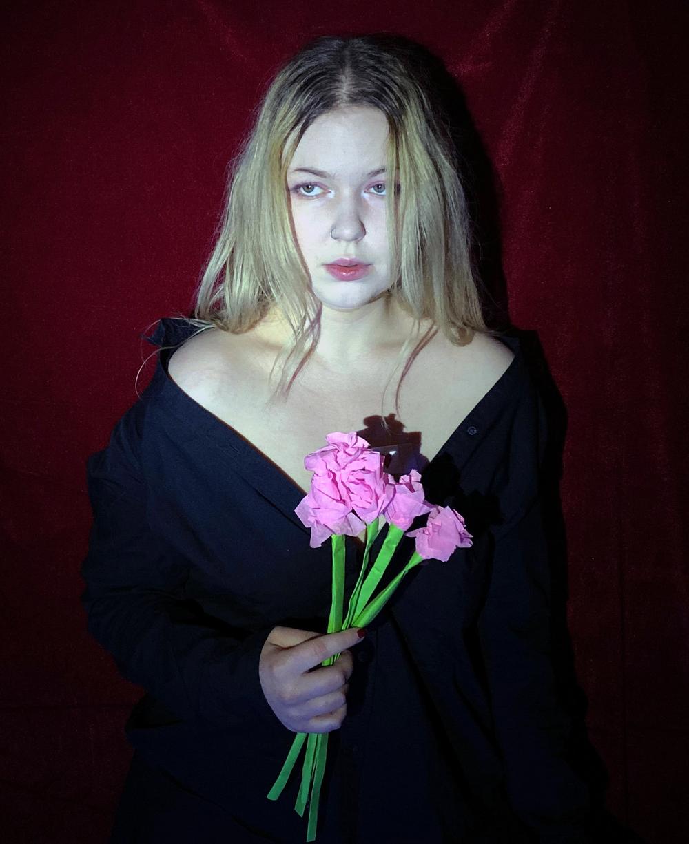 Standing in black against a red velvet backdrop, holding a small bunch of pink carnations