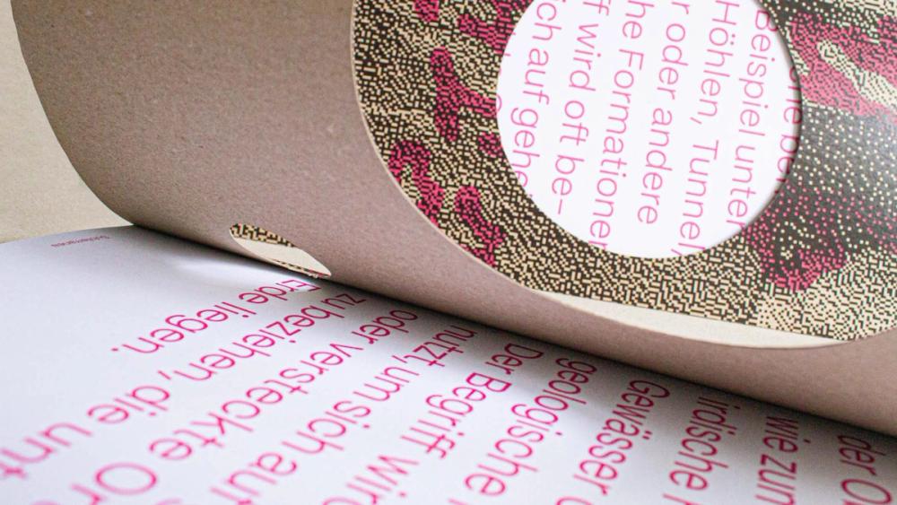 Close-up of a curling kraft page, its die-cut circle framing dithered pink halftone with text curving around the hole