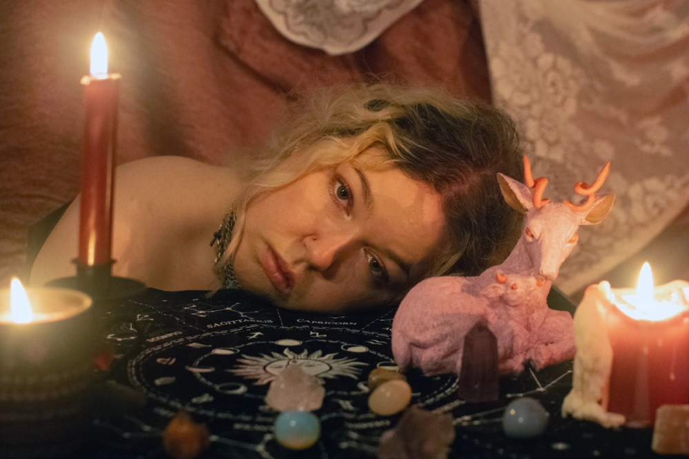 Head resting on an astrology cloth among candles, crystals and a pink felted stag, lit only by flame