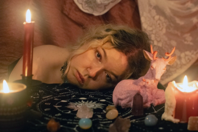 Head resting on an astrology cloth among candles, crystals and a pink felted stag, lit only by flame