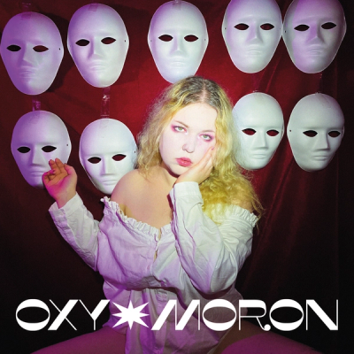 Blonde singer in a white off-shoulder blouse framed by ten blank white masks on red velvet, wordmark OXY MORON below
