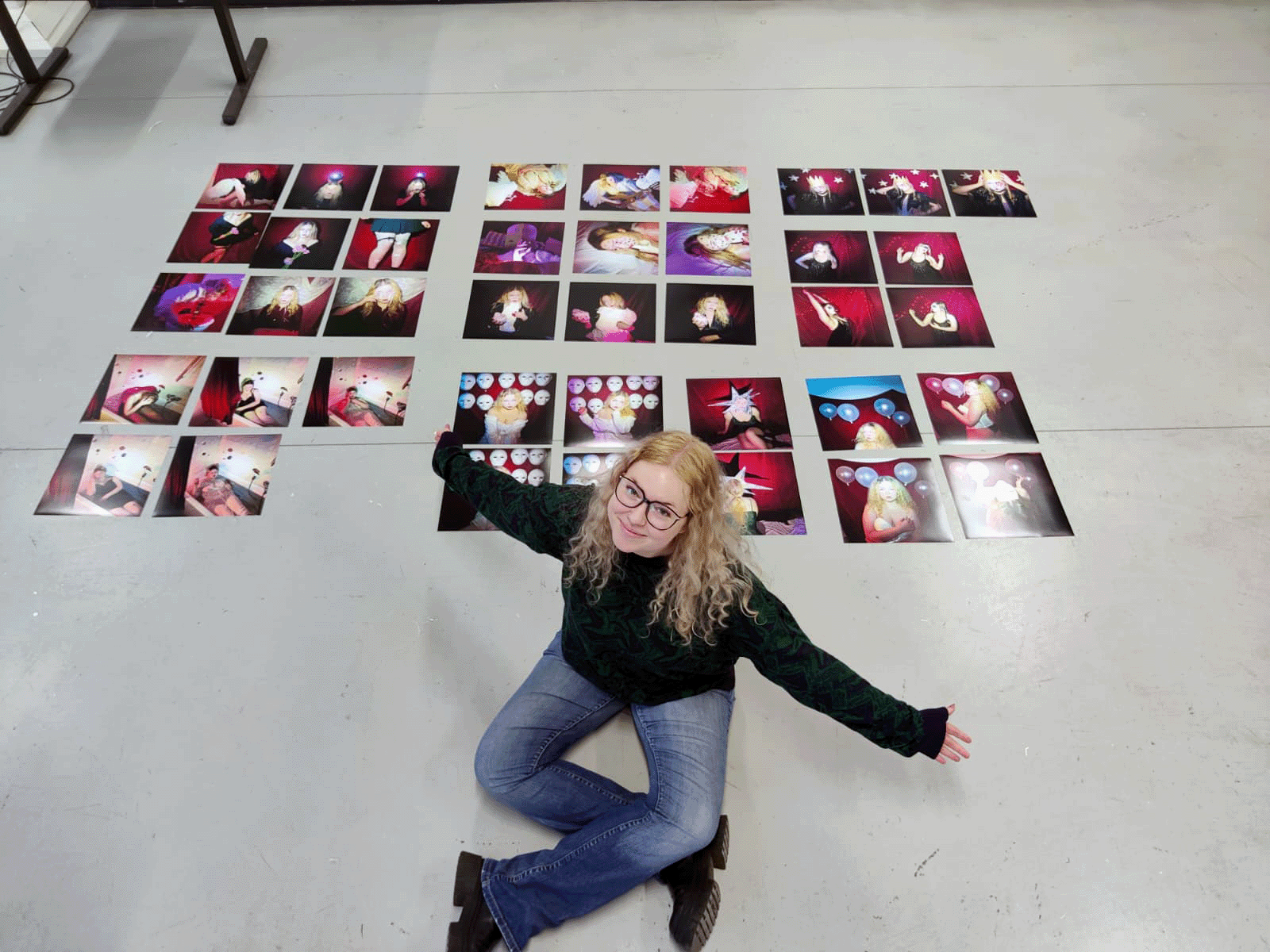 Overhead view of the artist kneeling on a studio floor beside dozens of small photo prints laid out in grids