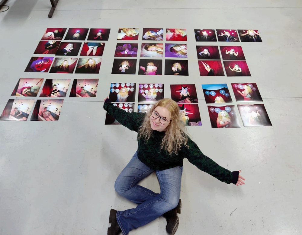 Overhead view of the artist kneeling on a studio floor beside dozens of small photo prints laid out in grids
