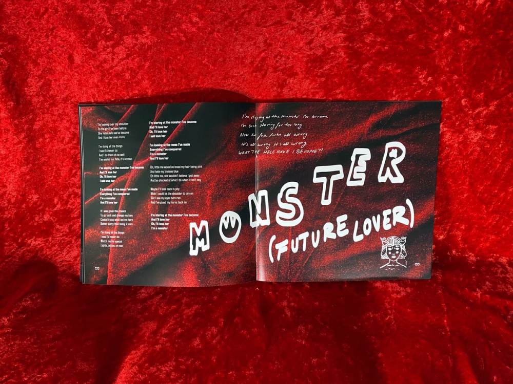 Open lyric booklet on red velvet, the spread titled Monster (Future Lover) in white marker lettering