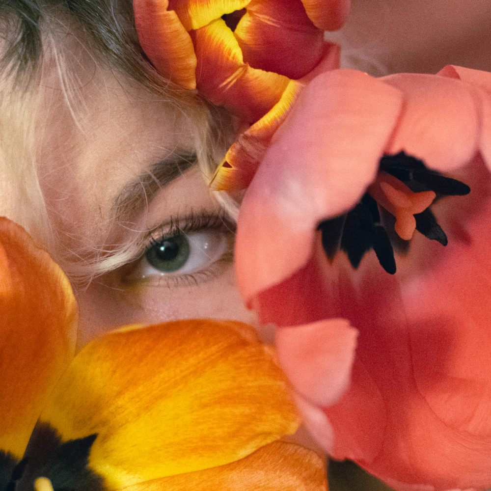 Tighter crop with a single green eye visible past a coral tulip whose black heart fills the right of the frame