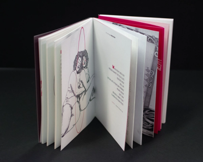 Hardcover book standing open on black, magenta-edged pages, ink drawing of two entwined figures