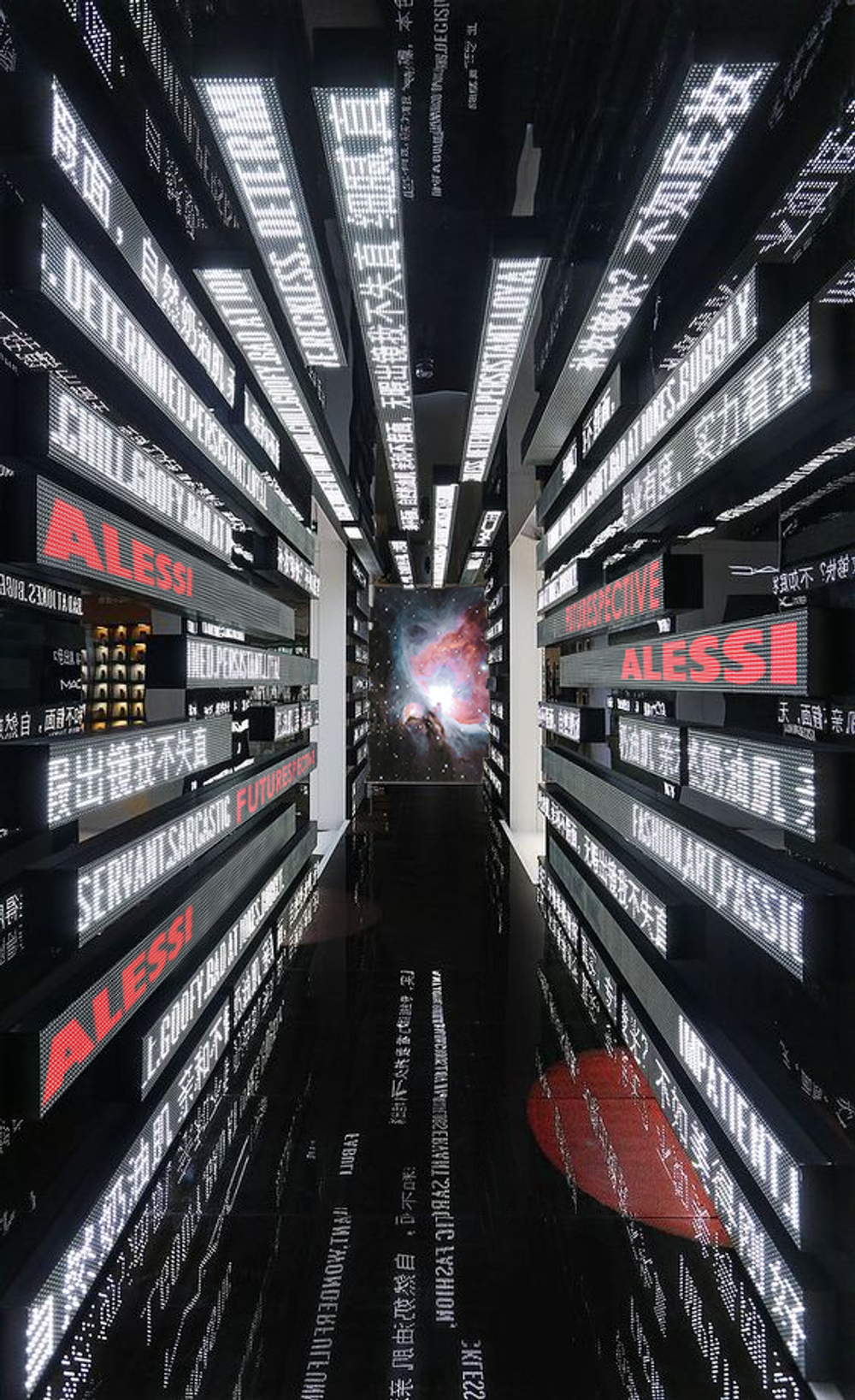 Narrow corridor clad in LED text panels, red ALESSI lettering glowing over a mirror-black floor toward a nebula screen