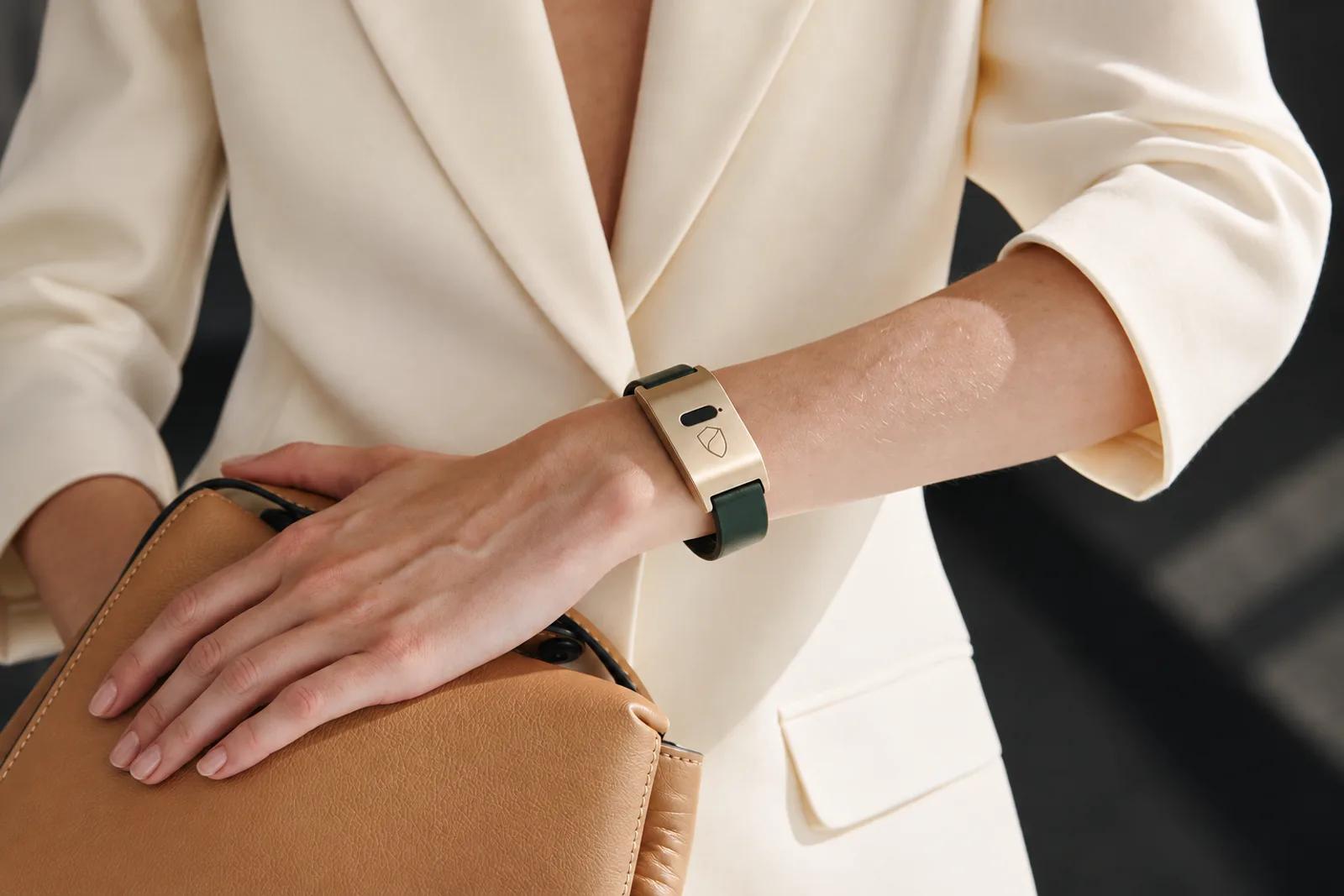 Close-up of the Brava Arc in champagne and forest green on a wrist, cream blazer and leather bag