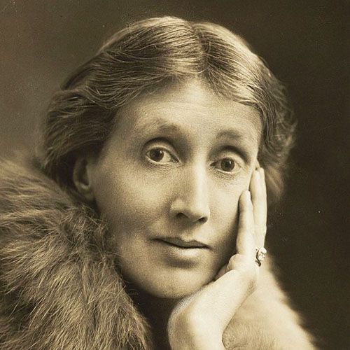 Un retrato en sepia de Virginia Woolf, mirando directamente a la cámara con una mano apoyada en su mejilla y luciendo un abrigo de piel.