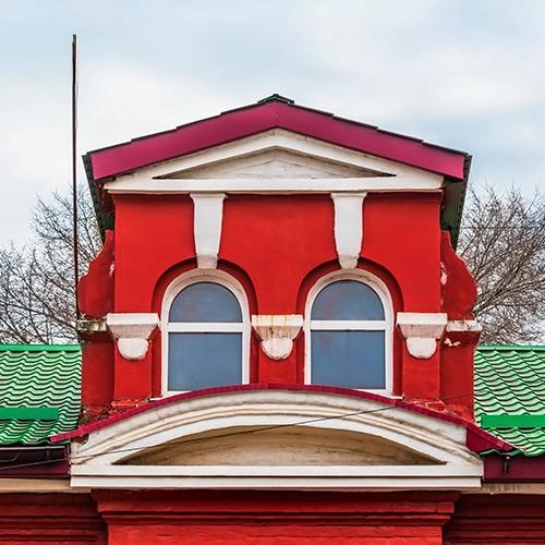 La fachada superior de un edificio rojo con dos ventanas arqueadas, detalles blancos y un techo verde.