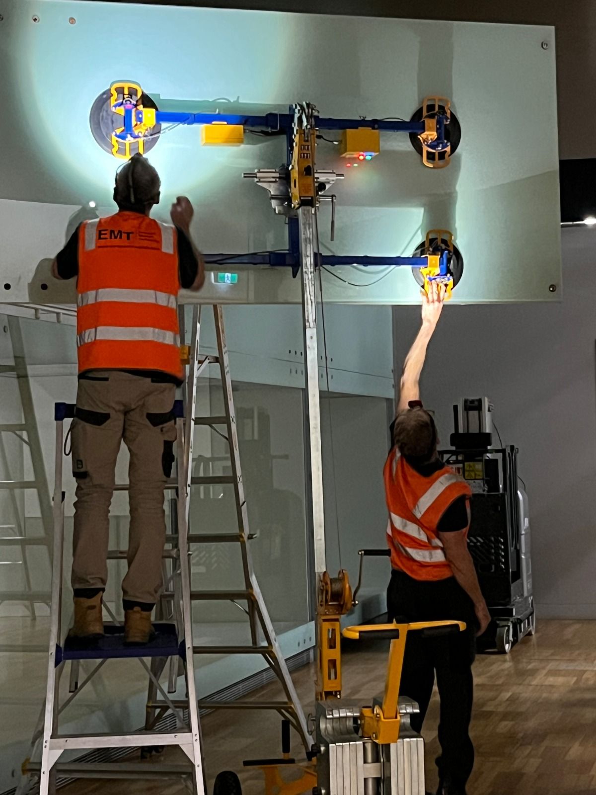 Quattrolifts powered vacuum lifter placing a large glass panel as art handlers work inside a museum gallery