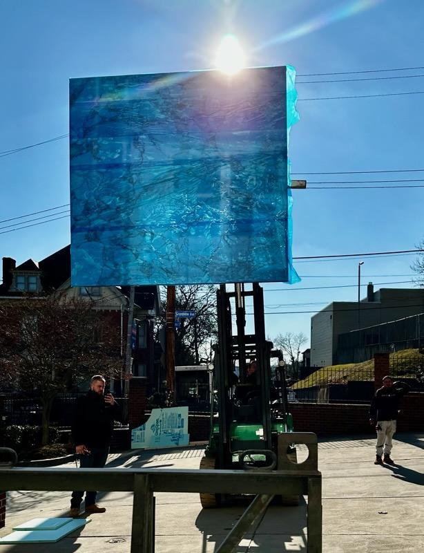 Quattrolifts Omni and forklift raising a film-wrapped glass panel on a city street install