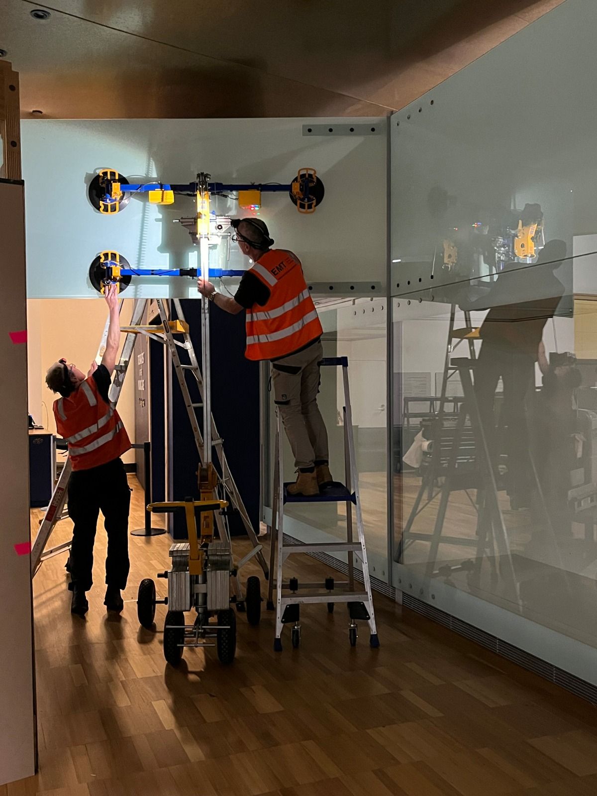 Quattrolifts vacuum lifter installing a tall glass partition as two installers work from ladders in a gallery