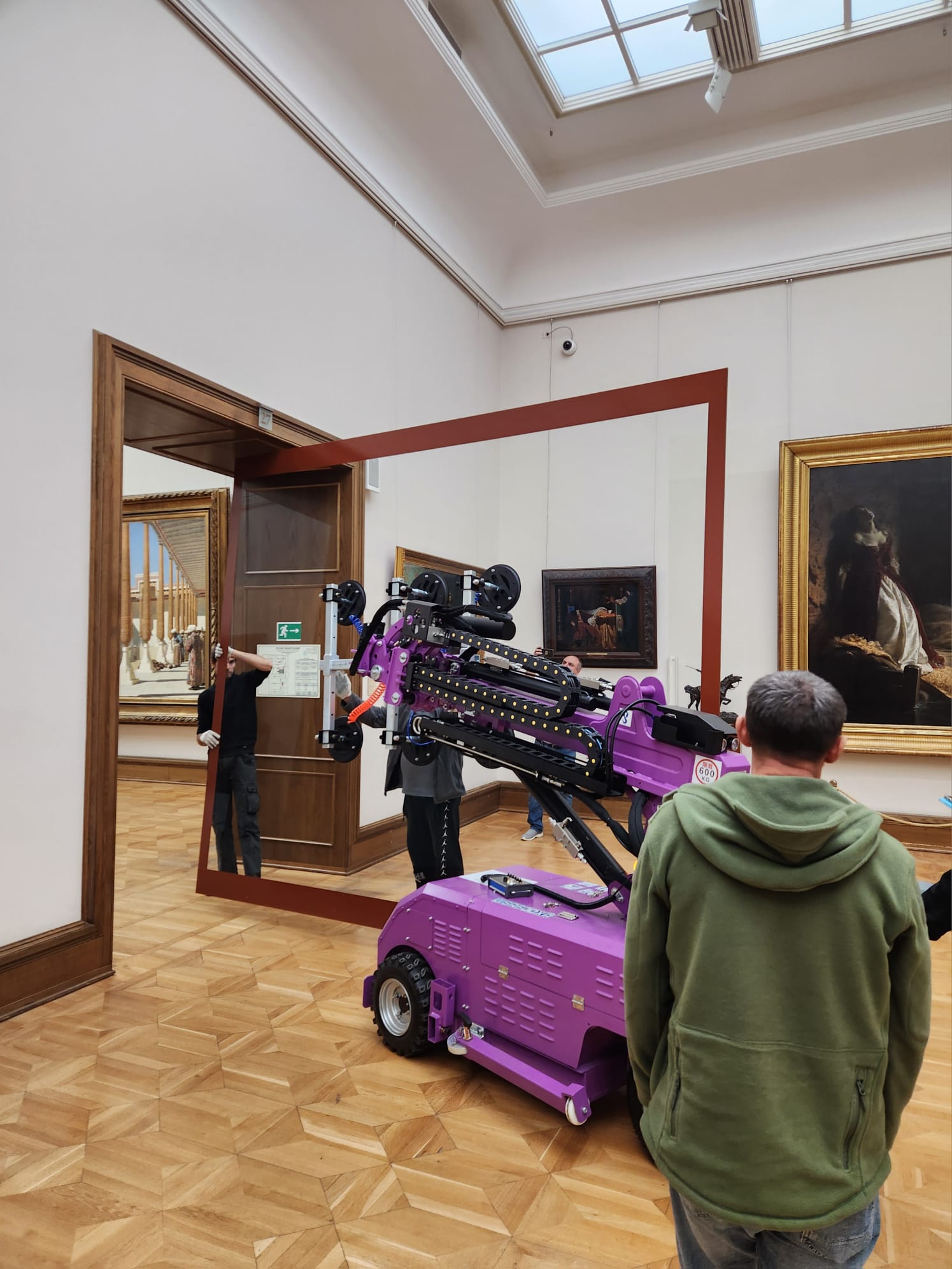 Quattrolifts vacuum lifter with raised arm working among framed paintings in a skylit museum gallery