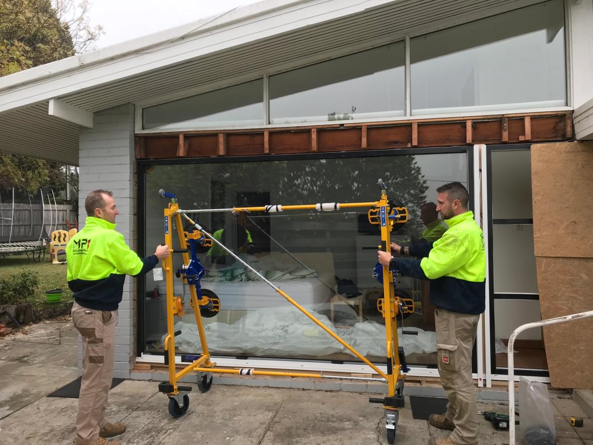 Installers set a large glass panel into a home opening with the Quattrolifts Nomad lifter