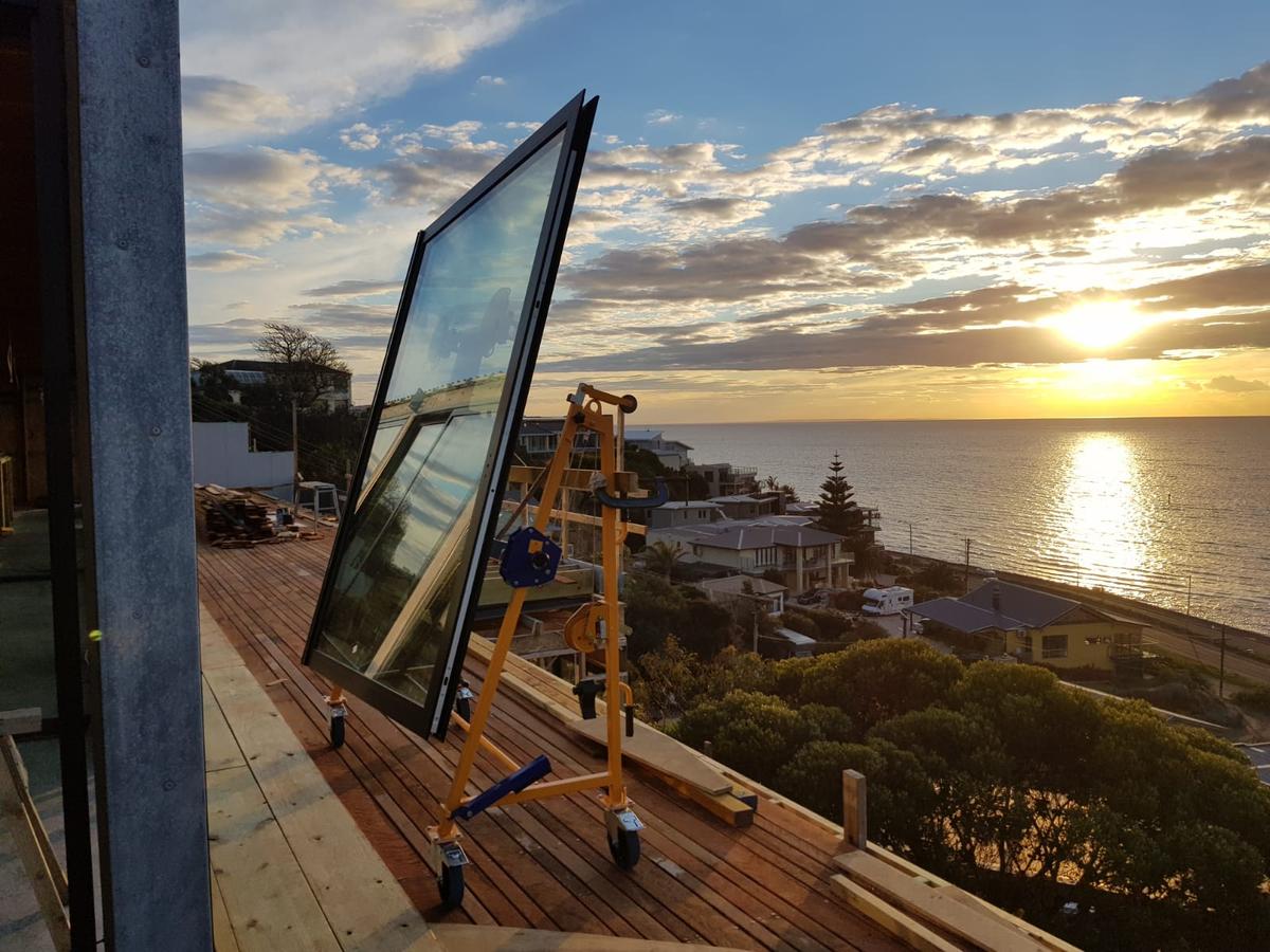 Quattrolifts Nomad lifter holding a large insulated glass unit on a coastal deck at sunset
