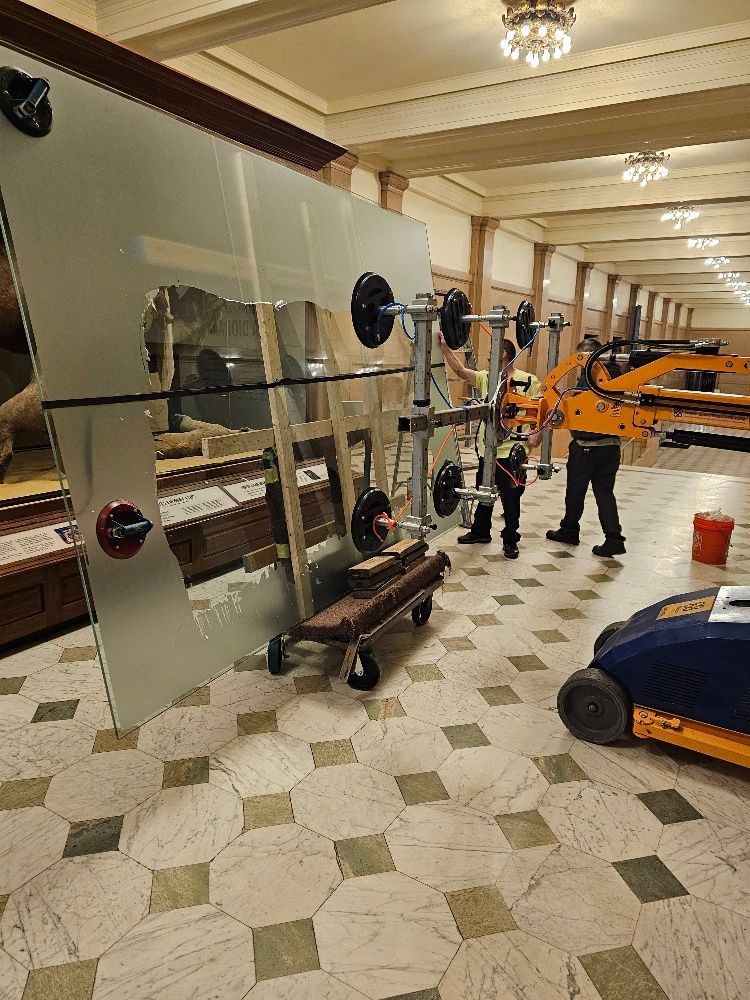 Quattrolifts vacuum lifter carrying a large glass display panel through an ornate museum hall with chandeliers