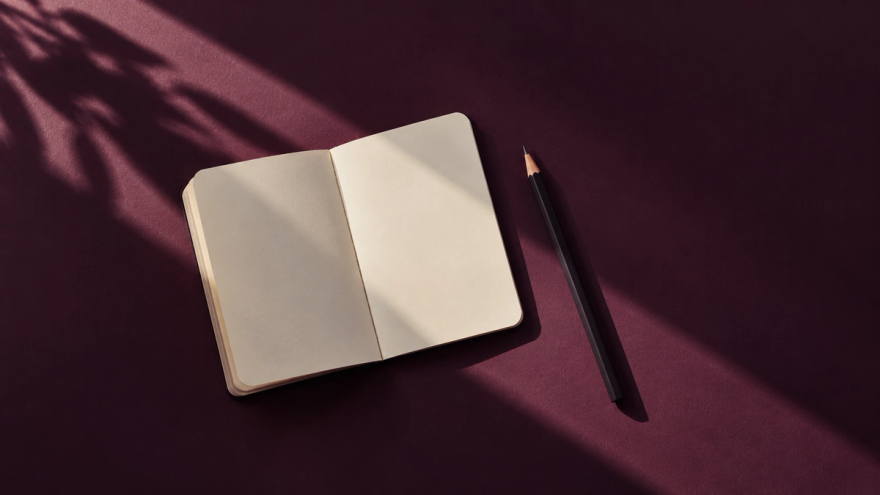 A blank pocket notebook and pencil cast crisp shadows on a deep plum surface.
