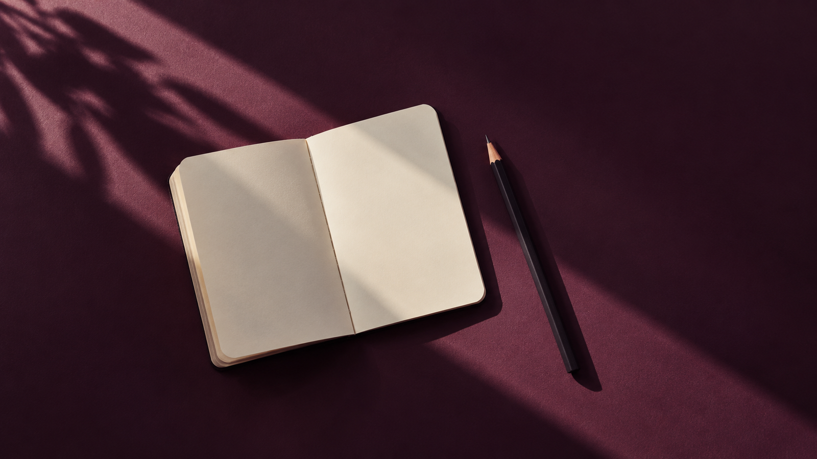A blank pocket notebook and pencil cast crisp shadows on a deep plum surface.