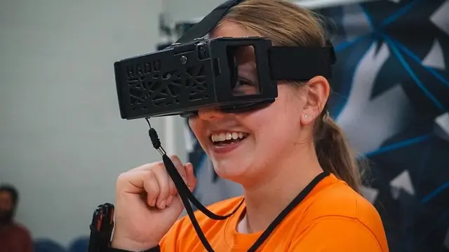 A smiling person wearing a HADO augmented reality headset during an indoor event.