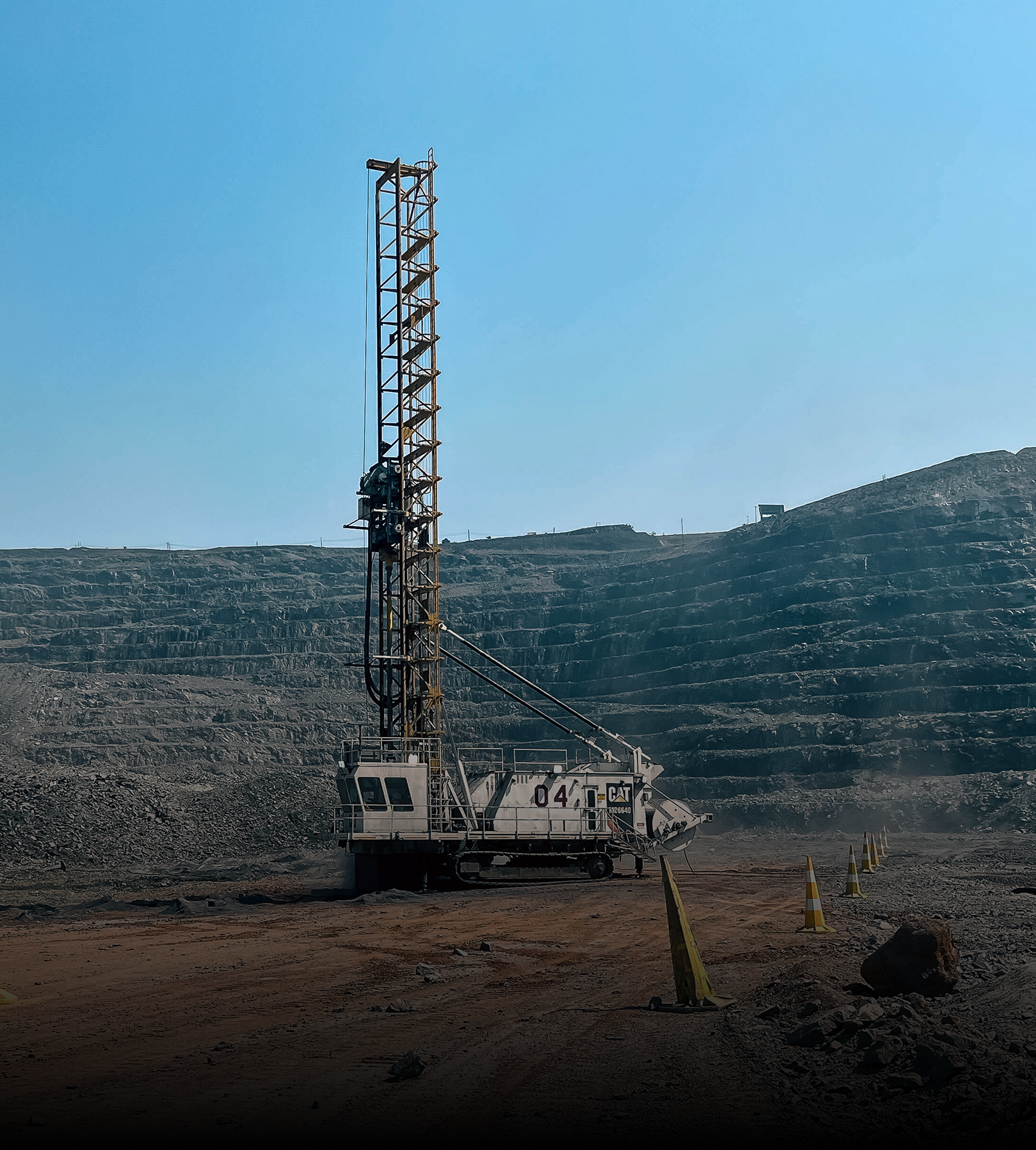 Cat 04 crawler drill rig operating in a terraced open-pit mine.