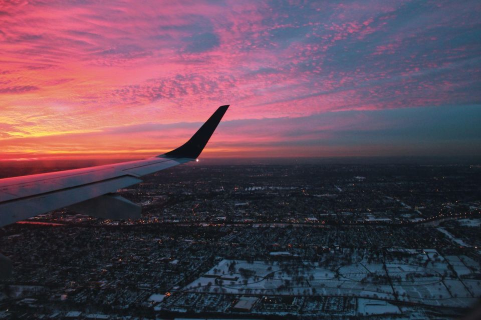 Airplane wing over a snowy city at sunset, with a vibrant pink and orange sky. Airplane wing over a snowy city at sunset, with a vibrant pink and orange sky.