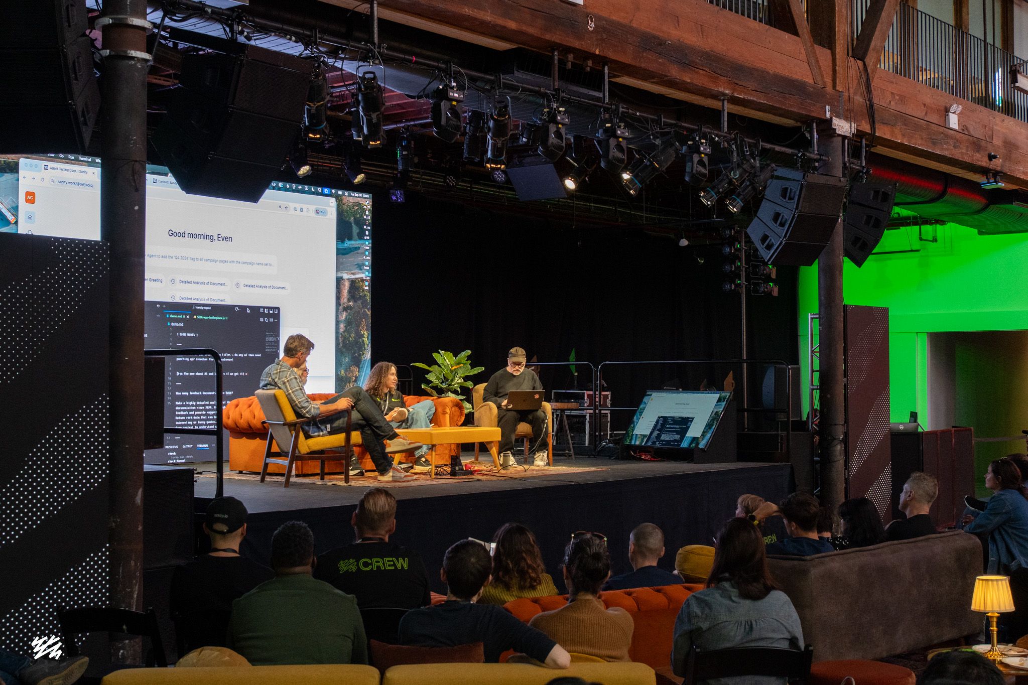 Even Westvang and Carolina Gonzalez demonstrating Sanity's Content Agent on stage at Everything NYC, with Magnus Hillestad and Simen Svale Skogsrud seated on orange sofas. Large screen on left displays the Content Agent interface greeting "Good morning, Even." Audience watches from sofas and chairs in foreground.