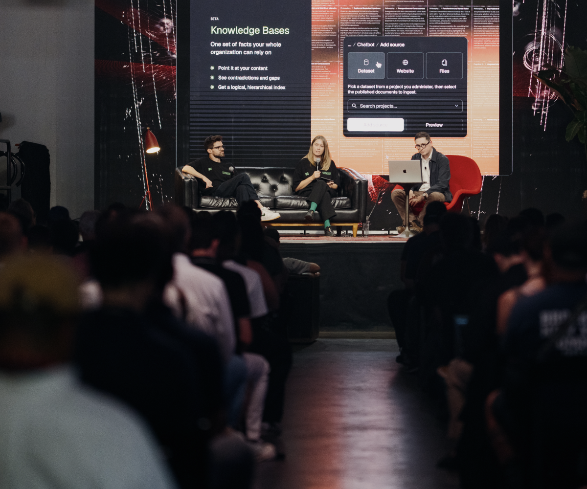 Three people on stage presenting a "Knowledge Bases" and chatbot interface on a large screen to an audience.